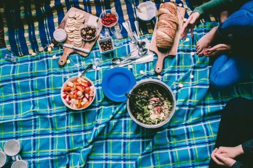 Picknick im Freien Vorbereitetes Essen in Schüsseln und auf Brettern auf einer blau-karierten Picknickdecke
