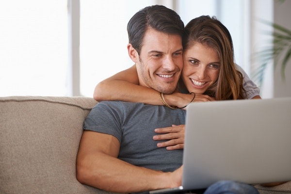 Frau schaut ihrem Mann, der am Laptop sitzt, über die Schulter