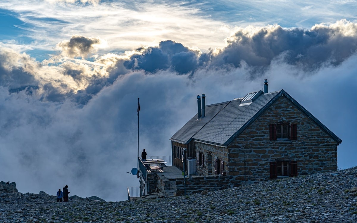 Menschen stehen um einer Berghütte bei Sonnenuntergang