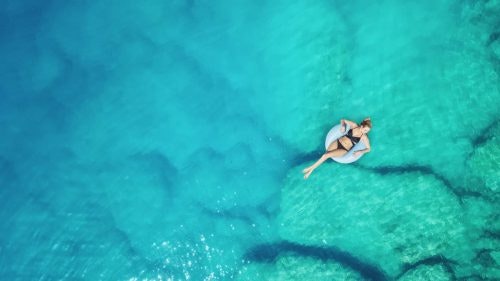 Eine Frau im Bikini treibt entspannt auf einem Schwimmring durch eine türkisblaue Bucht.