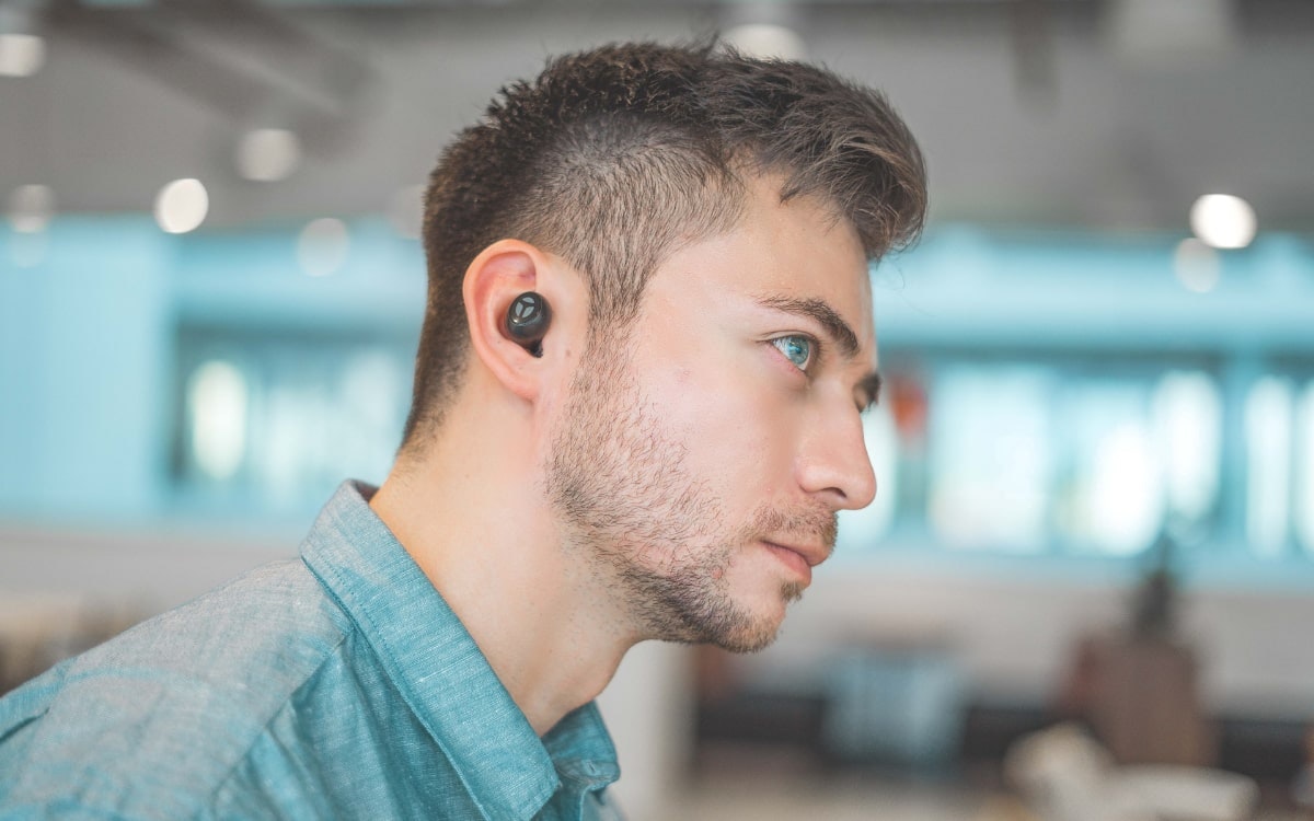 Mann mit blauem Hemd hat Wirless In-Ear-Kopfhörer im Ohr