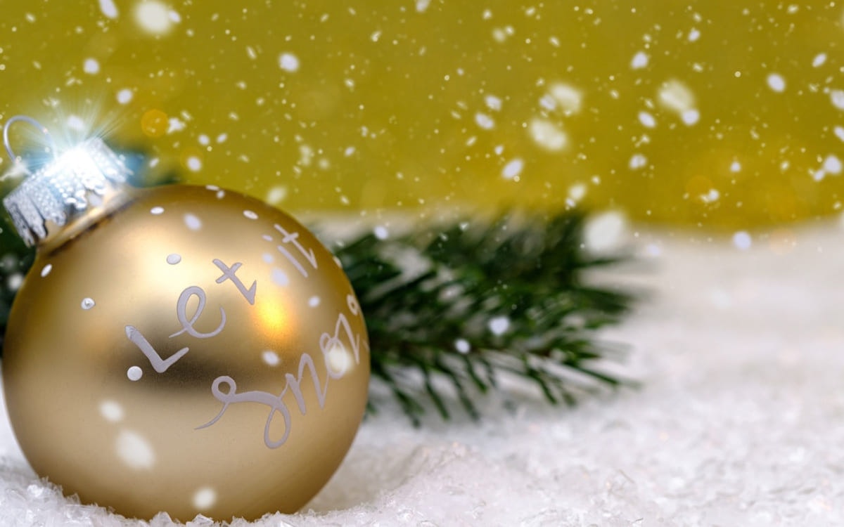Goldene Weihnachtskugel liegt im Kunstschnee neben Tannenzweig