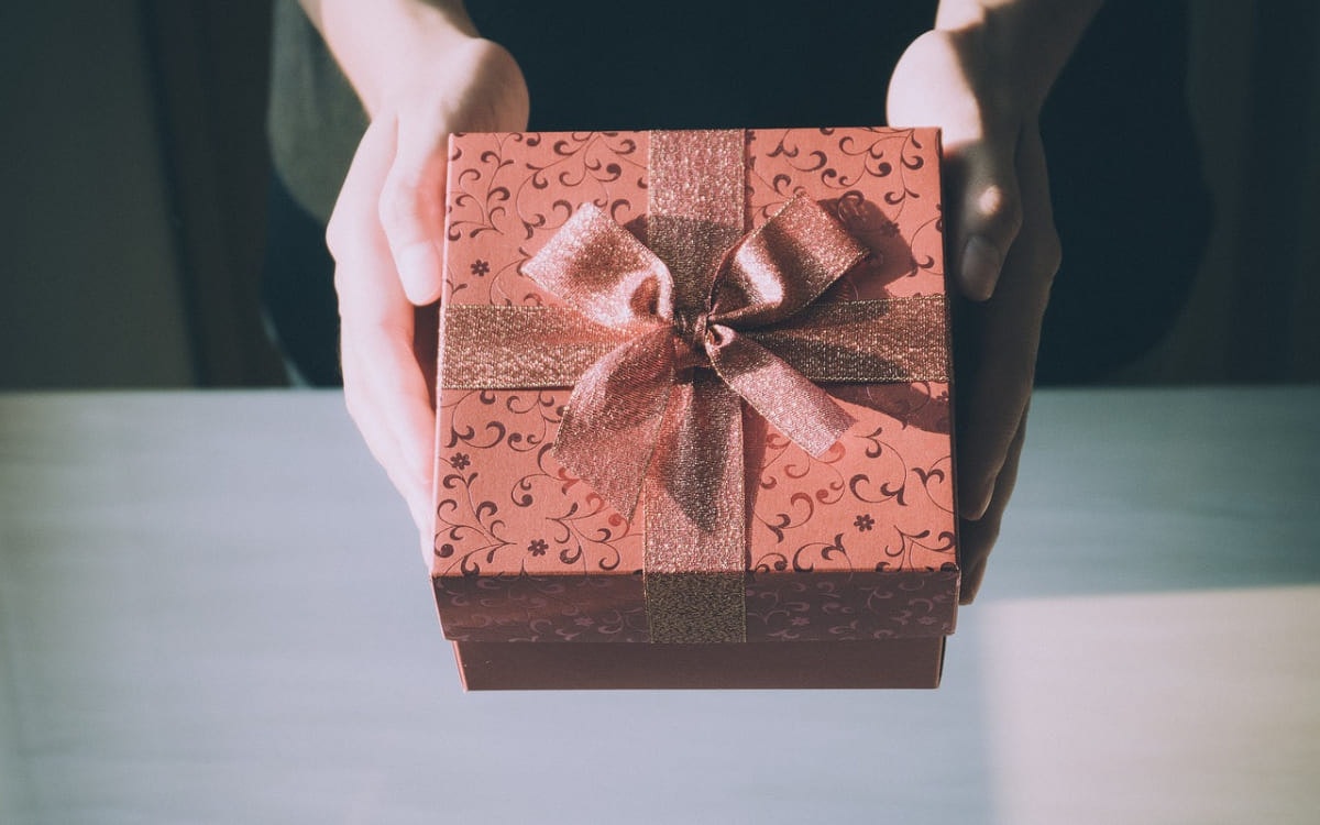 Roséfarbenes Geschenk mit Schleife in Frauenhänden
