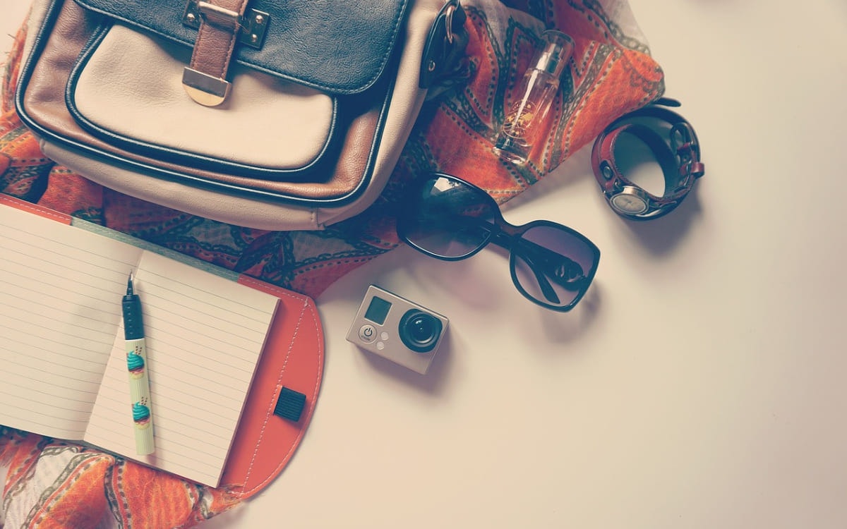 Tasche, Notizbuch, Kamera und Sonnenbrille liegen auf dem Tisch