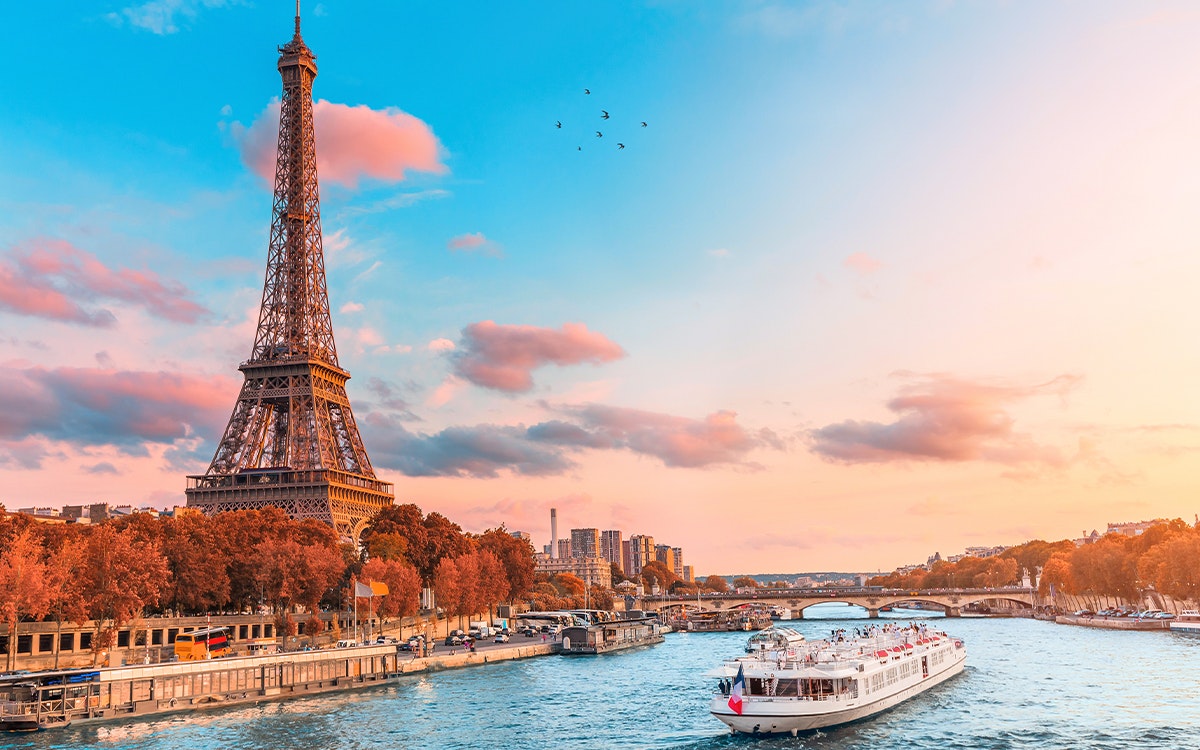 Die Seine im Abendrot, auf dem Fluss fährt ein Schiff, im Hintergrund befindet sich der Eiffelturm.